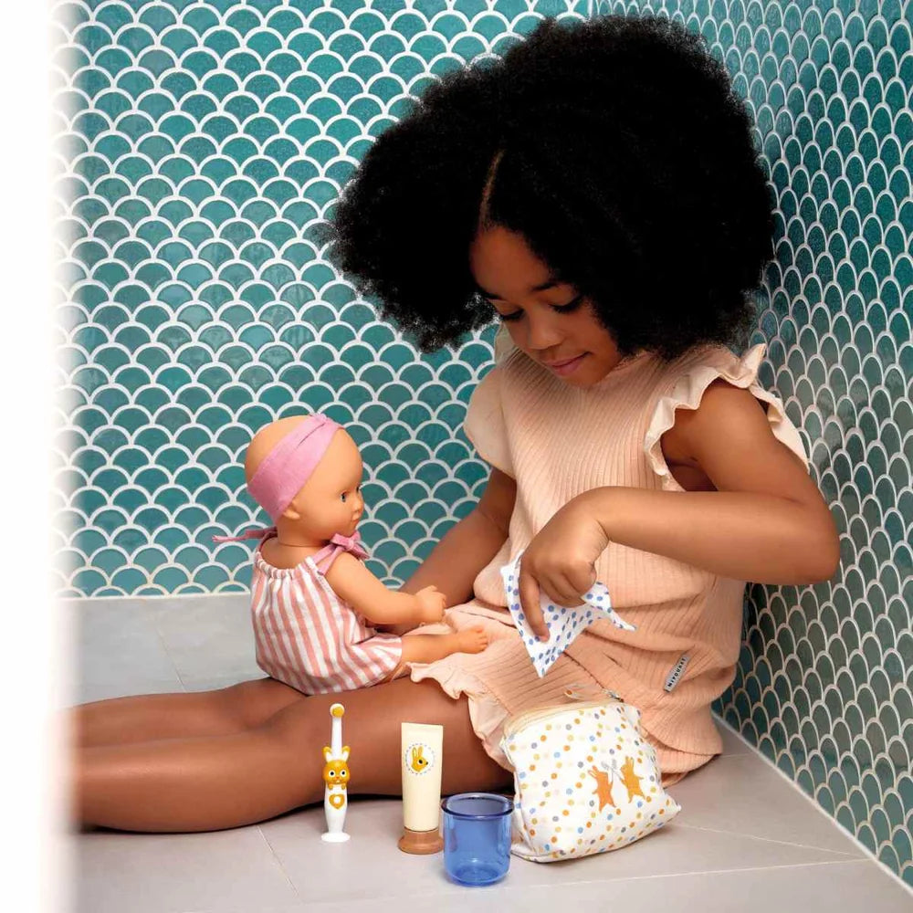 POMEA Badepuppe Mädchen Prune in rosa-weißem Kleid mit Mütze ; POMEA Badepuppe Mädchen Prune mit rosa Badeanzug und Stirnband ; POMEA Badepuppe Baby Prune 32cm mit rosa Outfit und Kopftuch ; POMEA Badepuppe Mädchen Prune liegt auf Wickelunterlage auf Tuch ; Kleines Mädchen mit POMEA Badepuppe in Rosa spielend auf Bett ; Mädchen mit POMEA Badepuppe in rosa Puppenkleidung spielend ; POMEA Badepuppe Mädchen Prune mit Zubehör beim Baden spielen