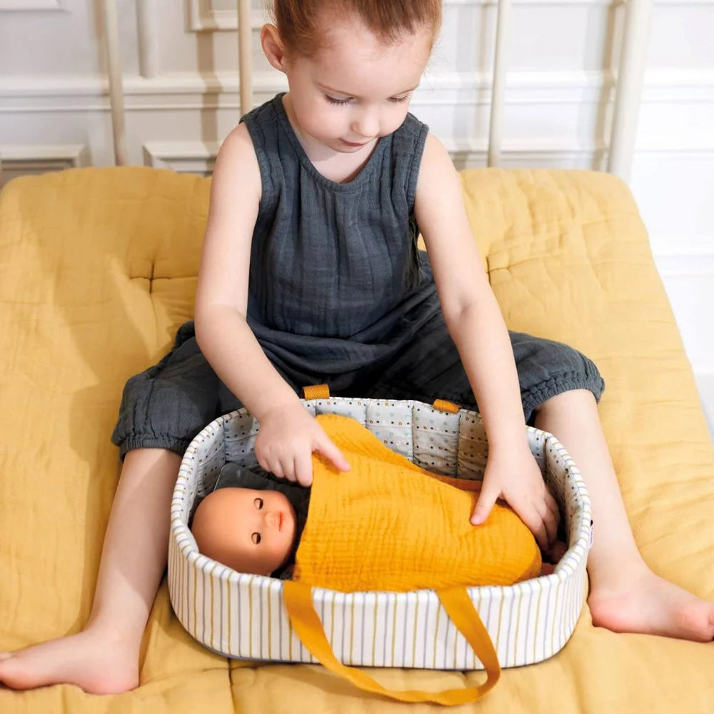 POMEA Puppentragetasche Blue Lines mit Puppe und Zubehör ; # POMEA Puppentragetasche mit orangenen Griffen und gestreiftem Design ; Kleines Kind mit POMEA Puppentragetasche Blue Lines und Puppe auf gelbem Sofa. ; POMEA Puppentragetasche Blue Lines mit Zubehör, Djeco Kollektion ; Puppentragetasche mit Puppe, gestreiftem Design und orangefarbenen Henkeln