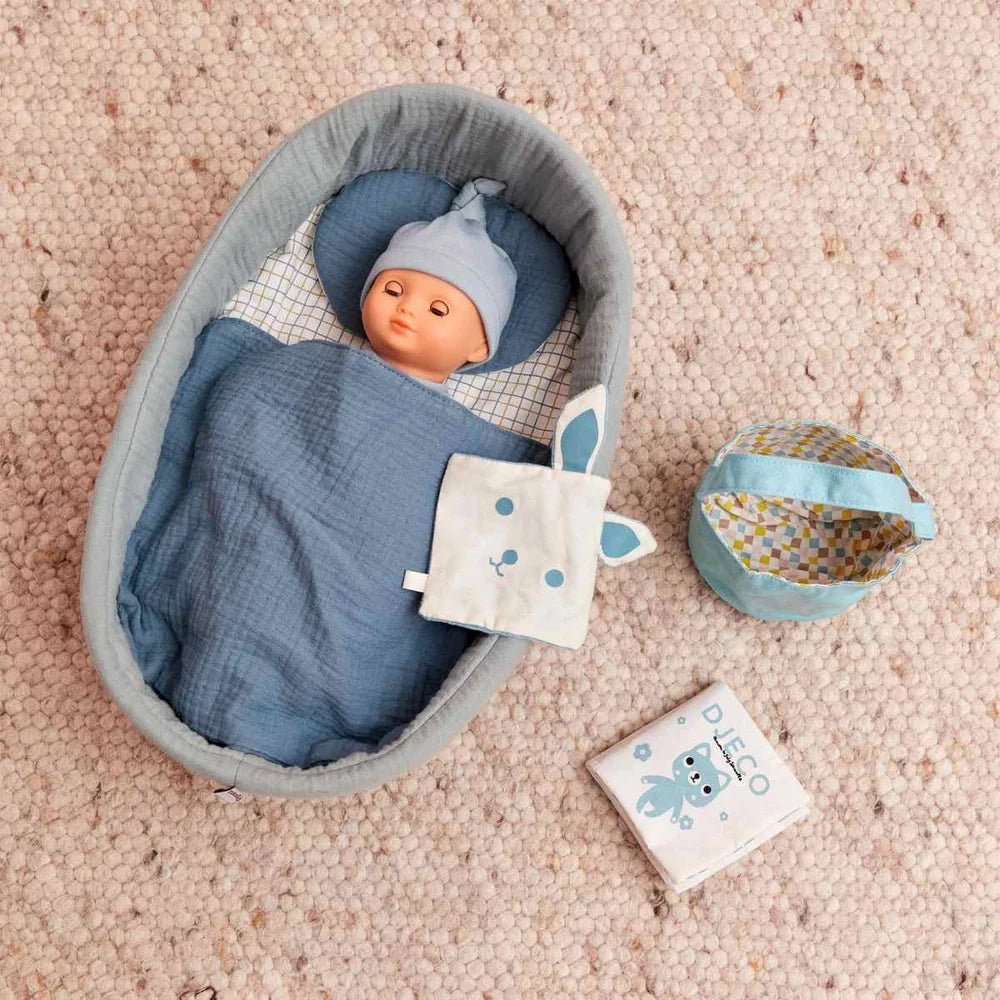 POMEA Puppe Neige mit weißem Strampler und türkisem Mütze sitzend ; POMEA Puppe Neige 32cm von Djeco mit grauer Mütze und weißem Body ; POMEA Puppe Neige - Babypuppe mit hellhäutiger Gesichtspartie, blauen Augen und kariertem Outfit ; POMEA Puppe Neige in grauem Bettchen mit Zubehör auf rosa Teppich