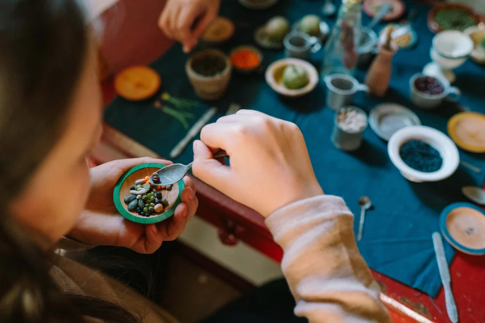 Kind mit grüner Grapat Schale füllt Spielzeuggeschirr mit Samen
