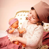 POMEA Badepuppe Mädchen Prune in rosa-weißem Kleid mit Mütze ; POMEA Badepuppe Mädchen Prune mit rosa Badeanzug und Stirnband ; POMEA Badepuppe Baby Prune 32cm mit rosa Outfit und Kopftuch ; POMEA Badepuppe Mädchen Prune liegt auf Wickelunterlage auf Tuch ; Kleines Mädchen mit POMEA Badepuppe in Rosa spielend auf Bett ; Mädchen mit POMEA Badepuppe in rosa Puppenkleidung spielend ; POMEA Badepuppe Mädchen Prune mit Zubehör beim Baden spielen