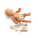 POMEA Puppe 3 Windeln mit bunten Mustern und Tiermotiven ; Pomea Puppe mit 3 waschbaren Windeln von Djeco ; POMEA Puppe 3 Windeln mit Katzen und Blumenmotiven in Creme ; POMEA Puppe sitzt mit Windel und Kleidung neben Windeln ; # POMEA Puppe mit drei farbenfrohen Windeln in Creme und Orange